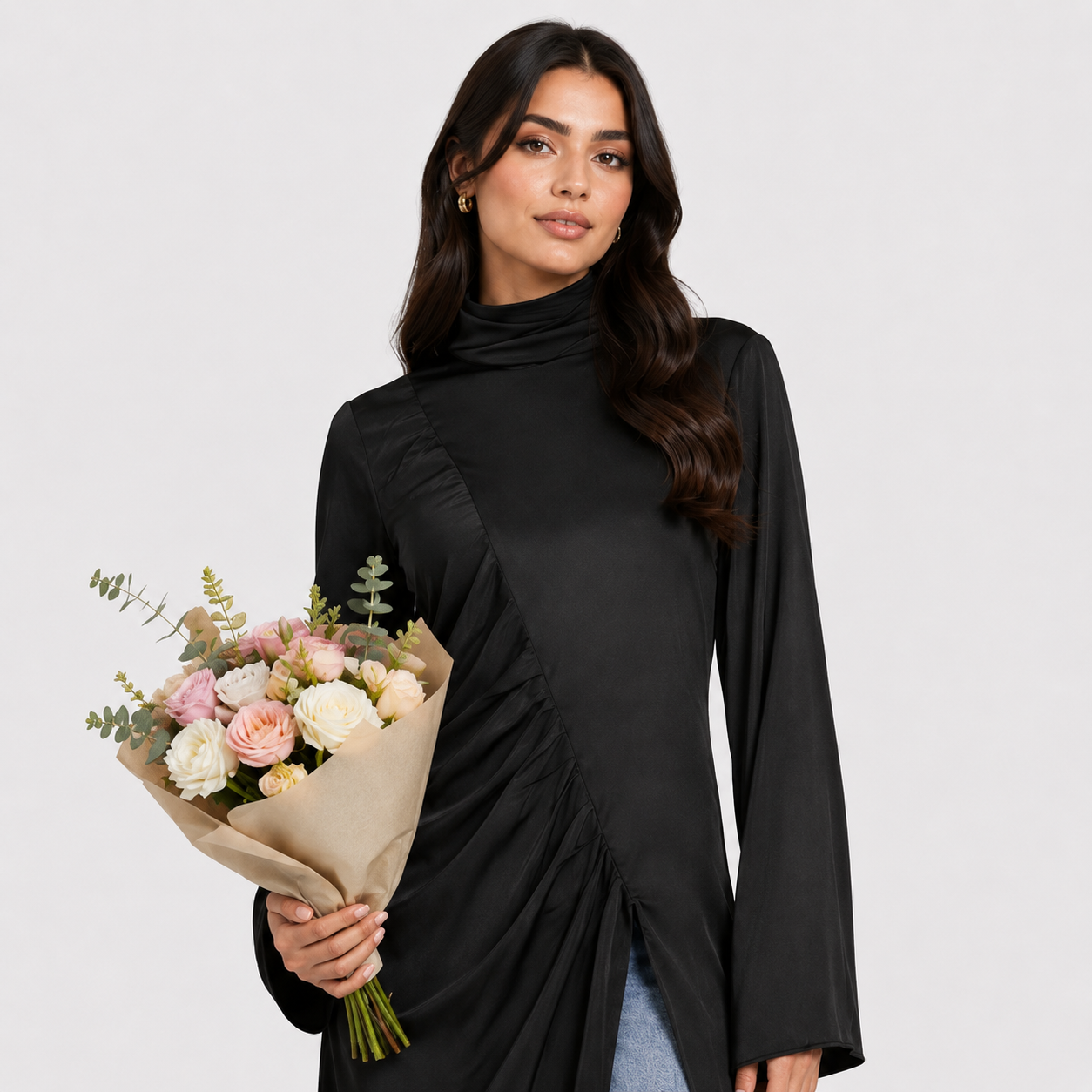 Woman wearing a black long-sleeve top and blue jeans with a black clutch against a white background