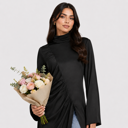 Woman wearing a black long-sleeve top and blue jeans with a black clutch against a white background