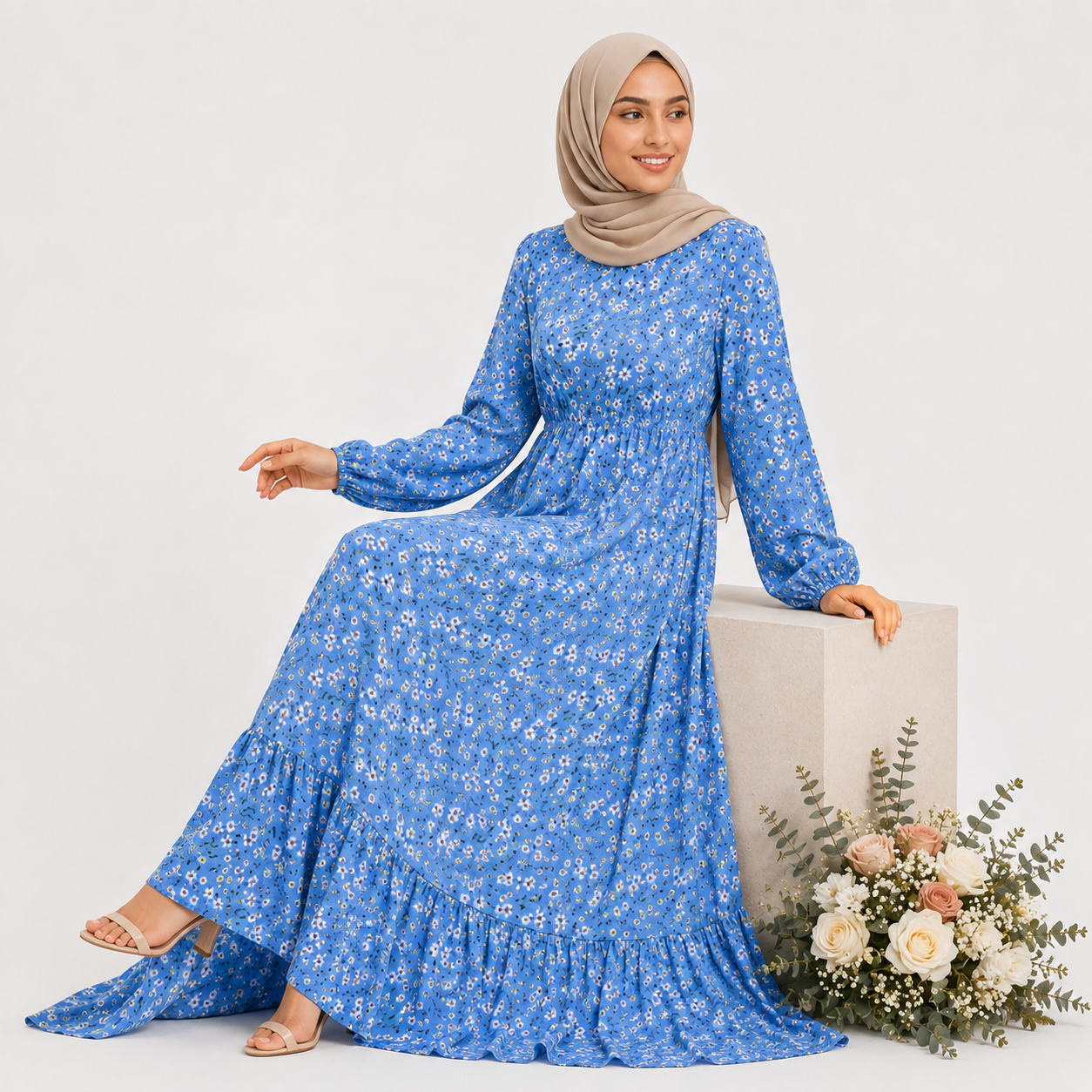 Woman wearing a blue floral dress and beige hijab holding a bouquet of flowers against a light gray background