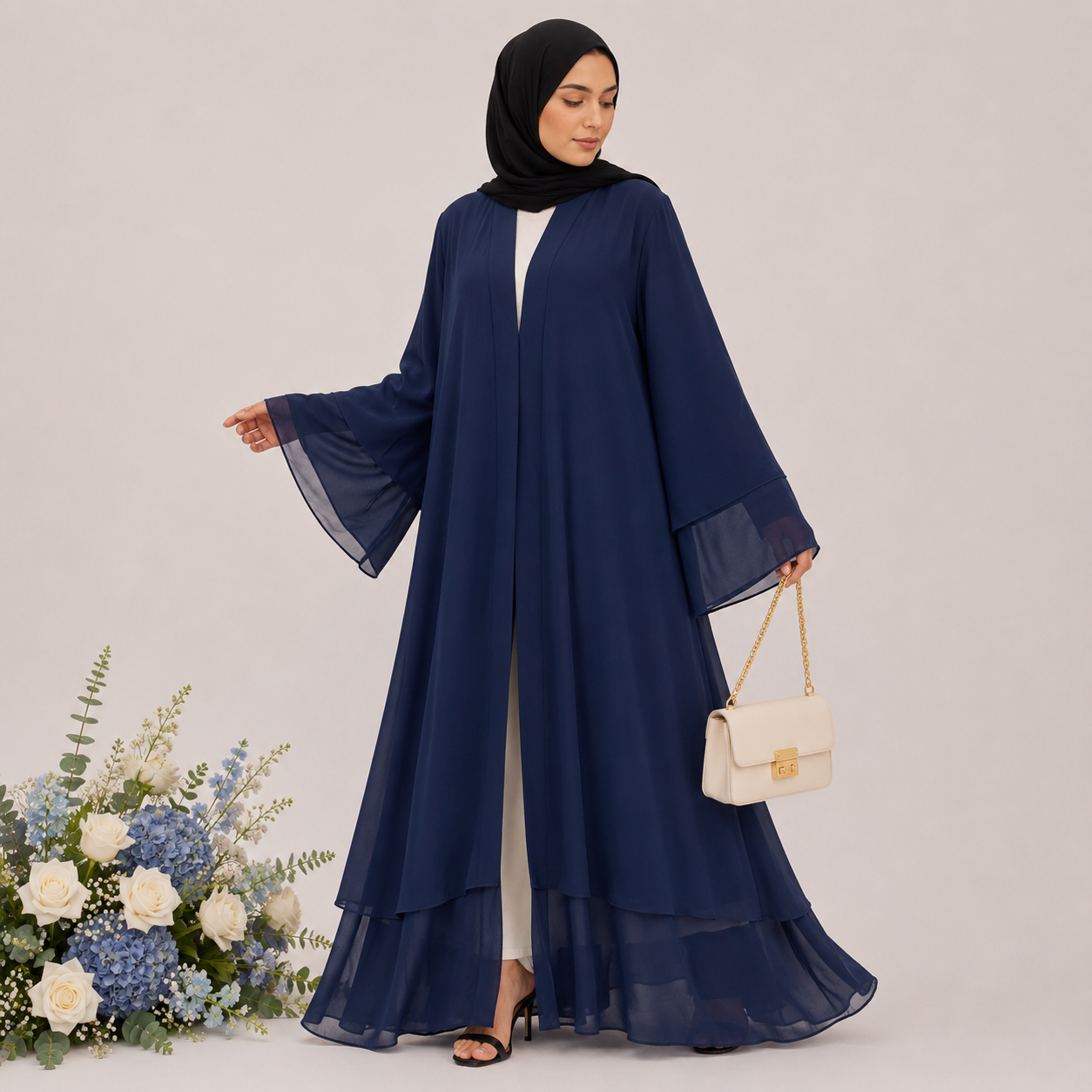 Woman wearing a navy blue abaya holding a white handbag with flowers on a light gray background