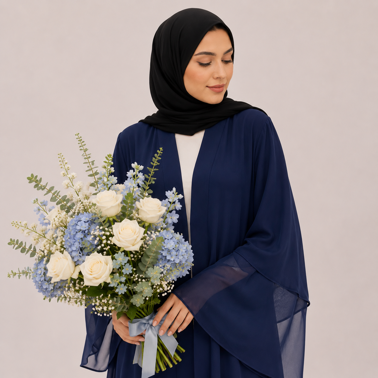 Woman wearing a navy blue hijab and holding a bouquet of flowers against a plain background
