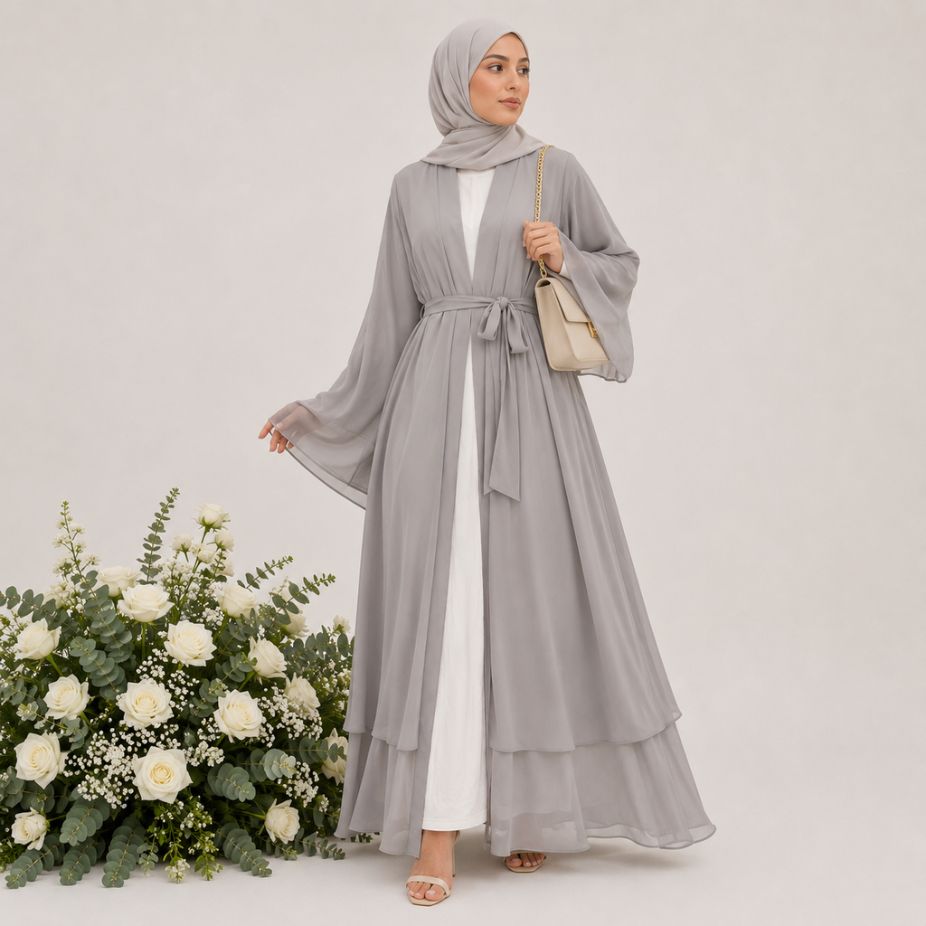 Woman in a long gray dress with a white background and floral arrangement.