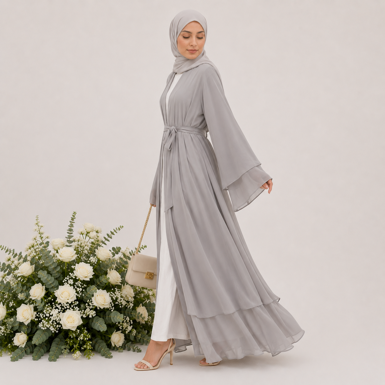 Woman in a gray dress with a hijab standing next to floral arrangements on a light background