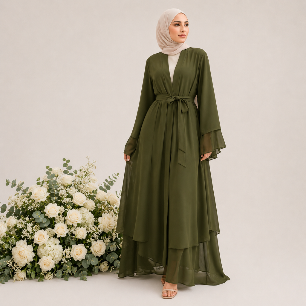 Woman wearing an olive green dress with a white hijab standing next to floral arrangements on a light background
