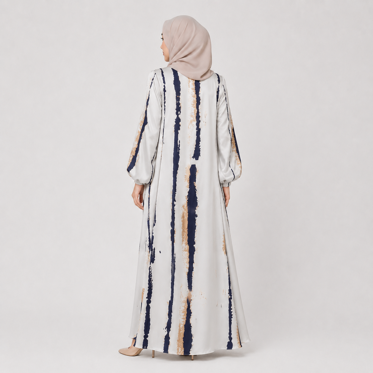Woman wearing a long, patterned dress with a hijab on a plain background