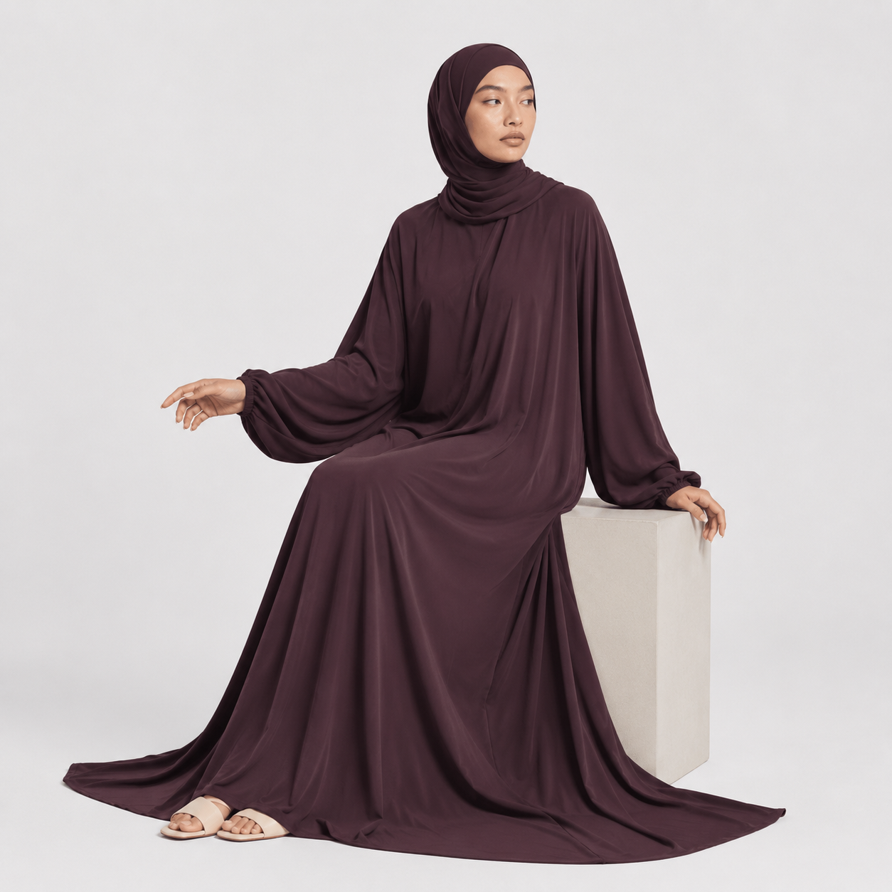 Woman wearing a dark brown hijab and dress on a white background