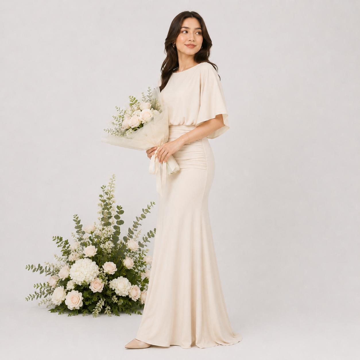 Woman in a long, light-colored dress holding flowers against a plain background
