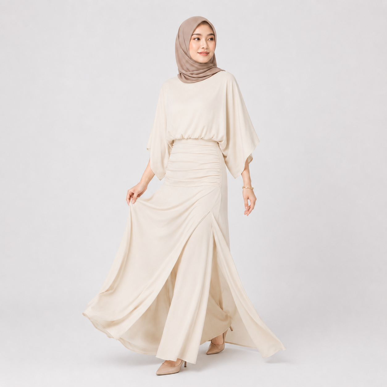 Woman wearing a long, flowing beige dress with a matching hijab on a light gray background