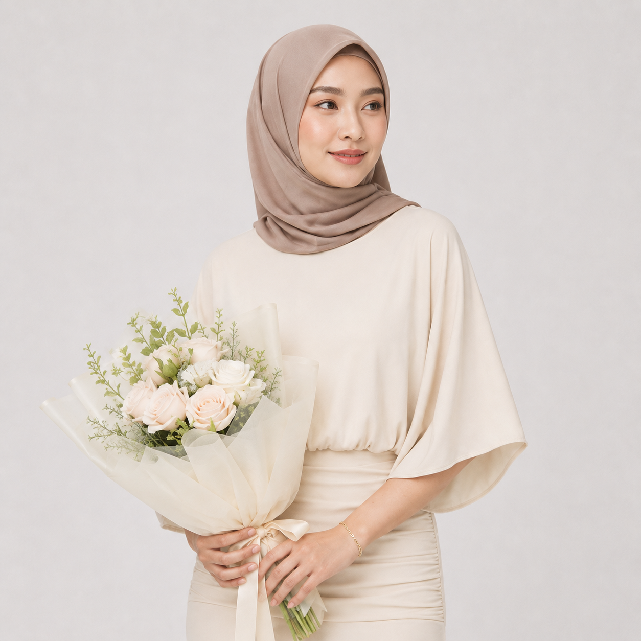 Woman wearing a beige hijab and dress holding a bouquet of flowers against a light gray background