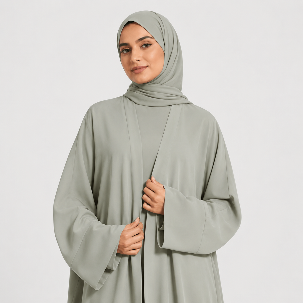 Woman wearing a light gray abaya and hijab on a white background