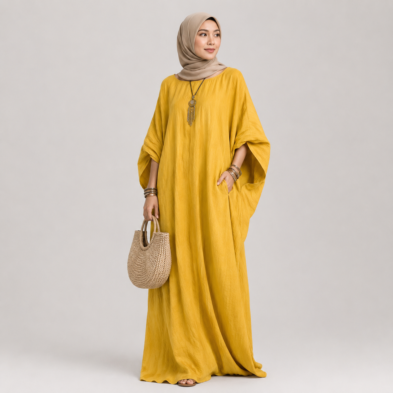 Woman wearing a mustard yellow dress holding a woven bag on a plain background