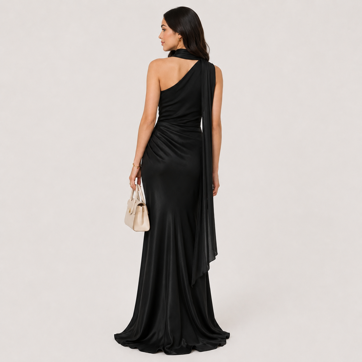 Woman in a black one-shoulder dress holding flowers and a clutch against a plain background
