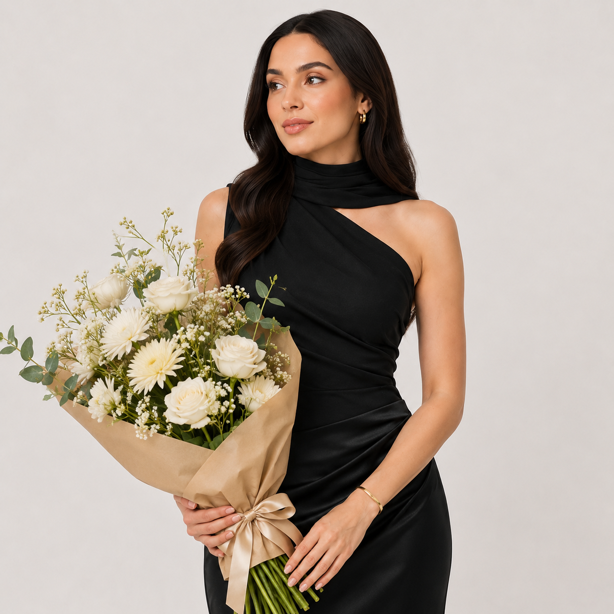 Woman in a black one-shoulder dress holding flowers and a clutch against a plain background