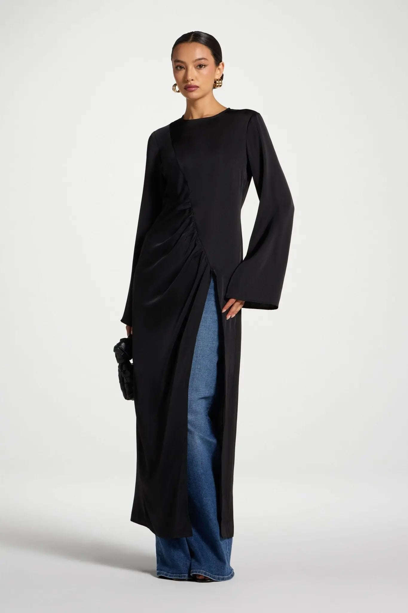 Woman wearing a black long-sleeve dress with a slit, standing against a white background