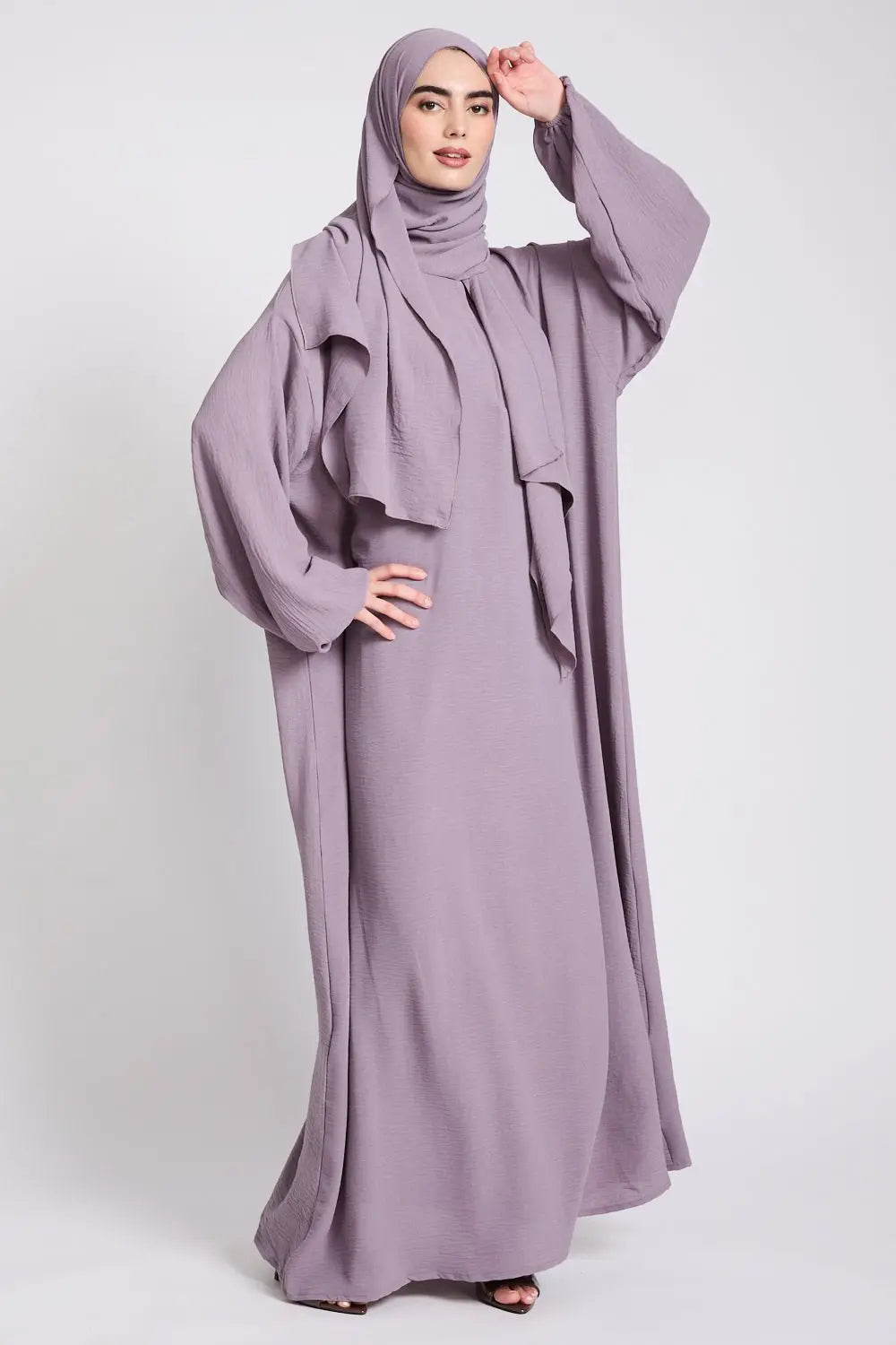 Woman wearing a long, light purple abaya with a matching hijab on a white background
