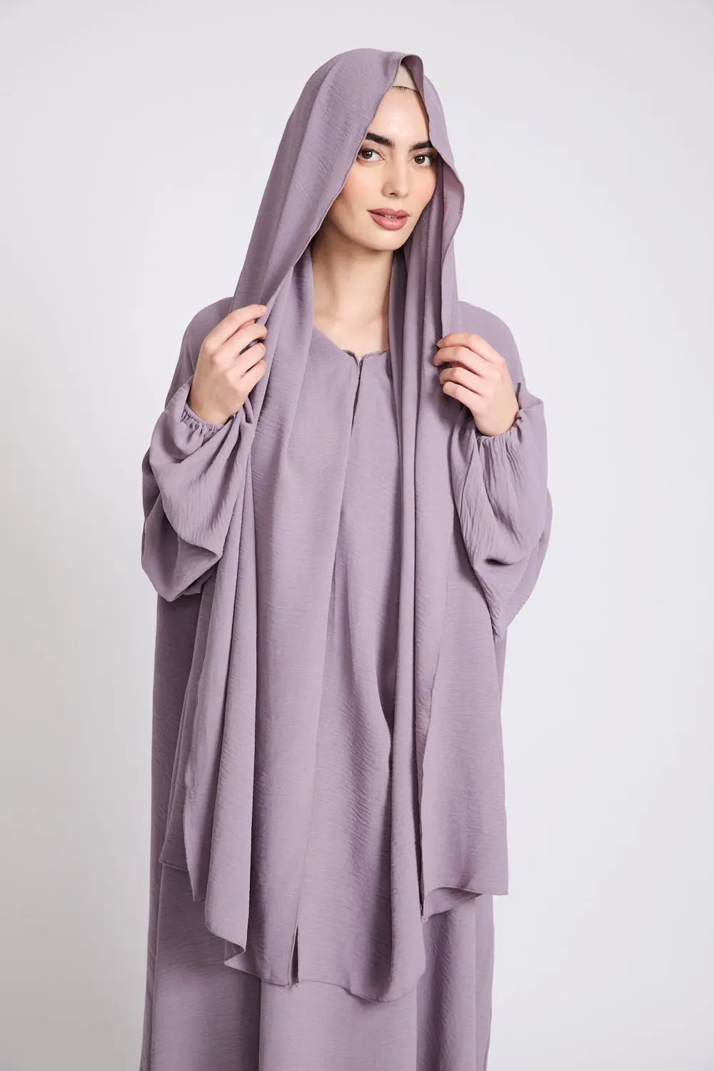 Woman wearing a light purple outfit with a matching hijab on a white background
