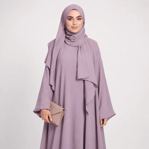 Woman wearing a light purple abaya with a matching hijab on a white background