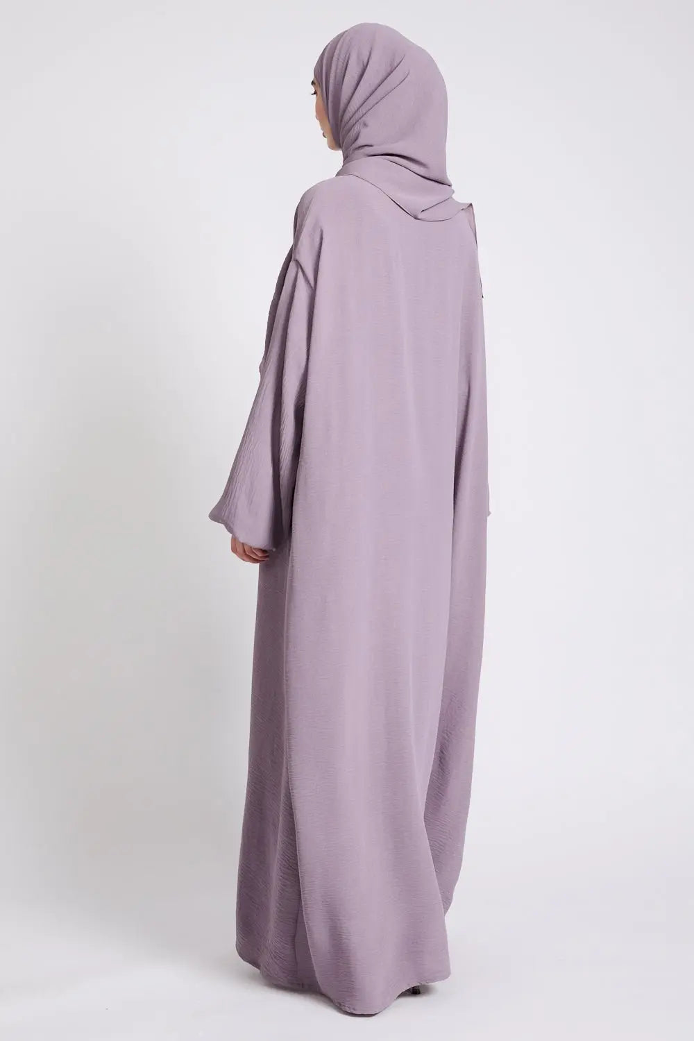 Person wearing a long, light purple abaya with a matching hijab on a white background