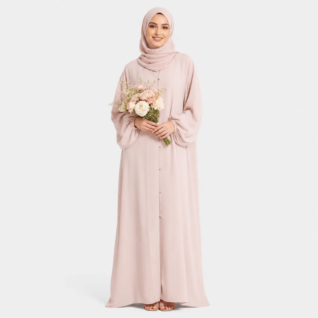 Woman wearing a light pink abaya holding flowers on a white background