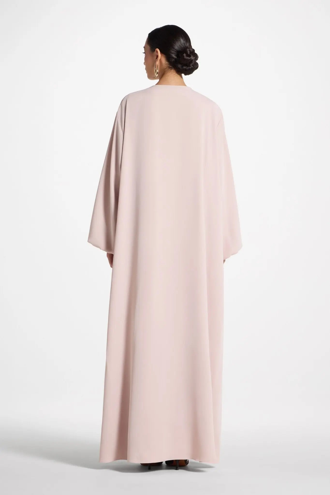 Woman wearing a long, light pink dress with a cape on a white background