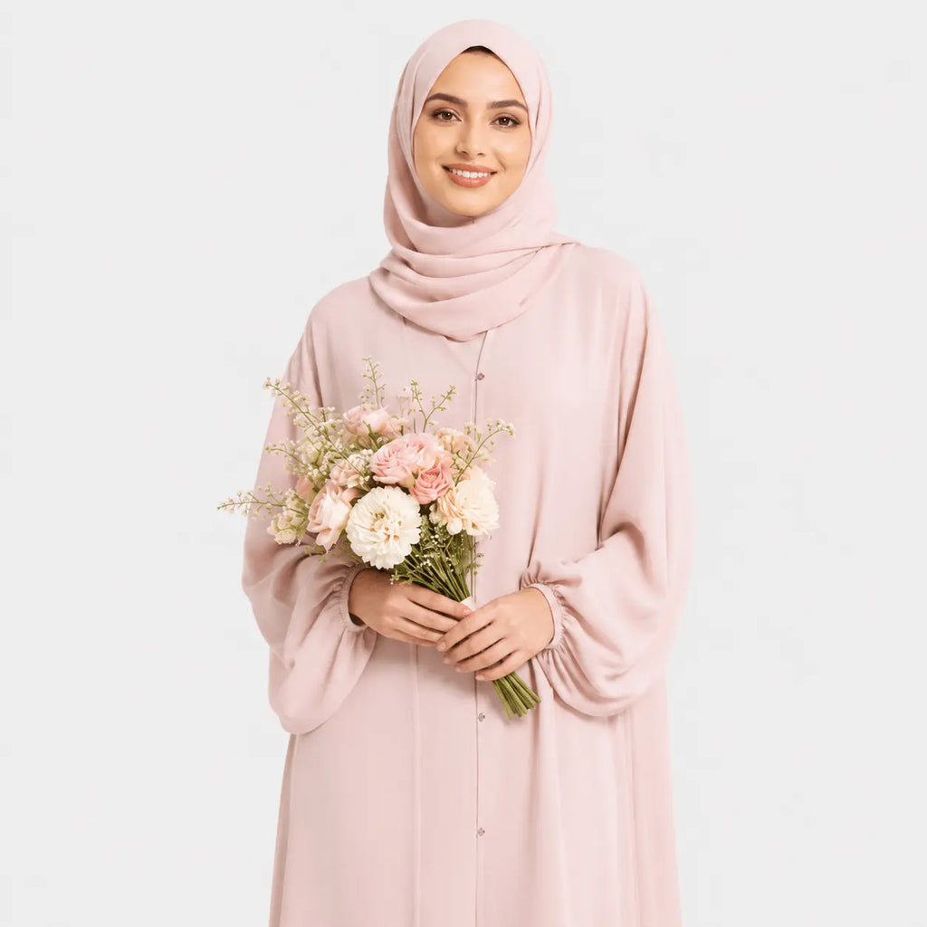 Woman wearing a pink hijab and dress holding a bouquet of flowers on a light gray background