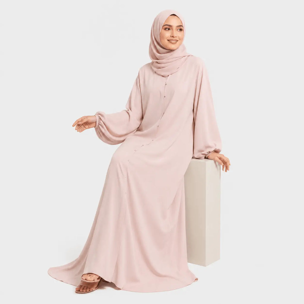 Woman wearing a pink abaya and hijab on a white background