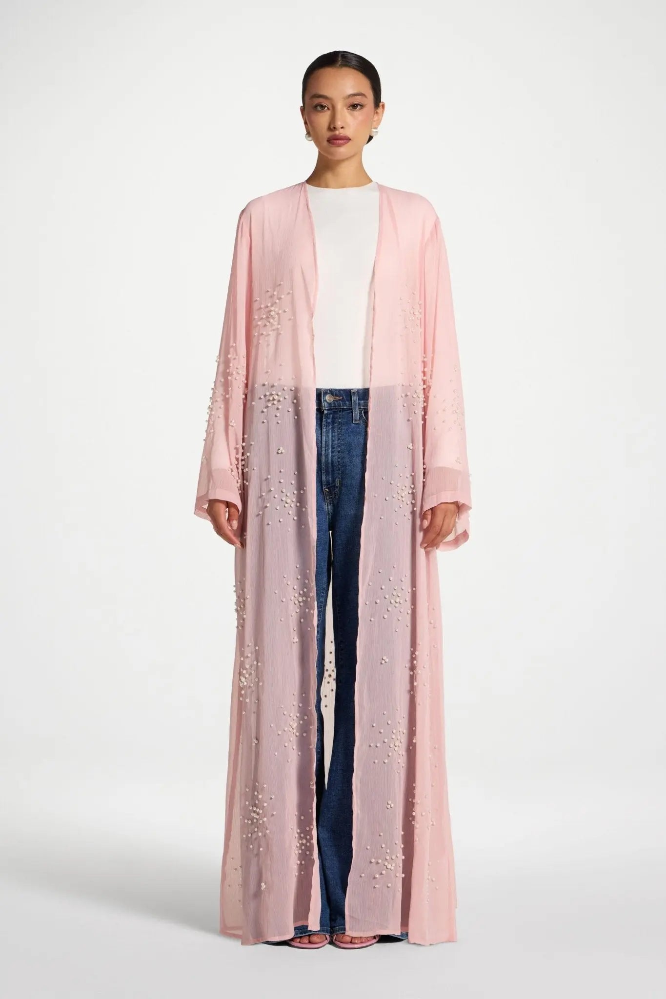 Woman wearing a long pink embroidered jacket on a white background