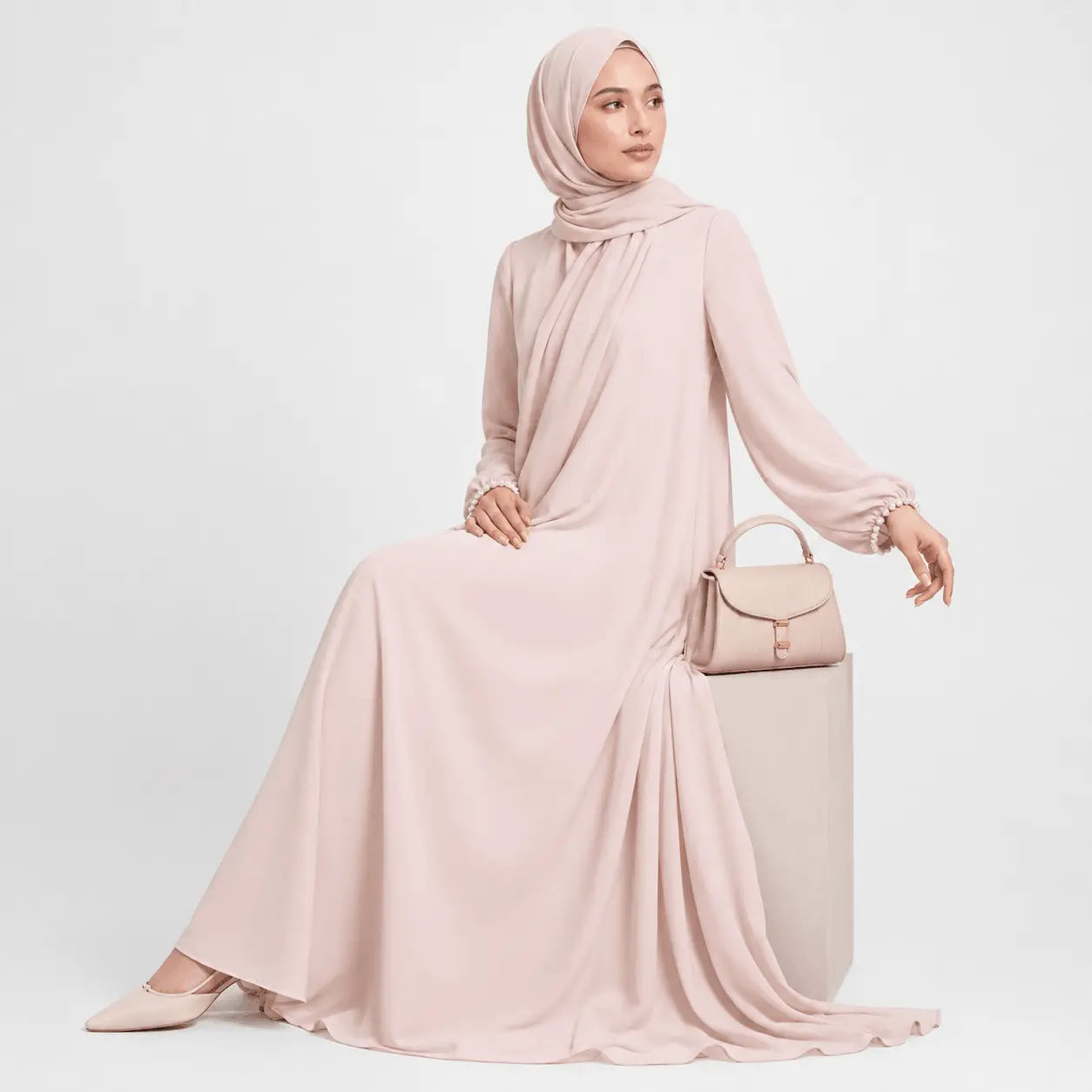 Woman wearing a long pink dress and hijab holding a matching handbag on a white background
