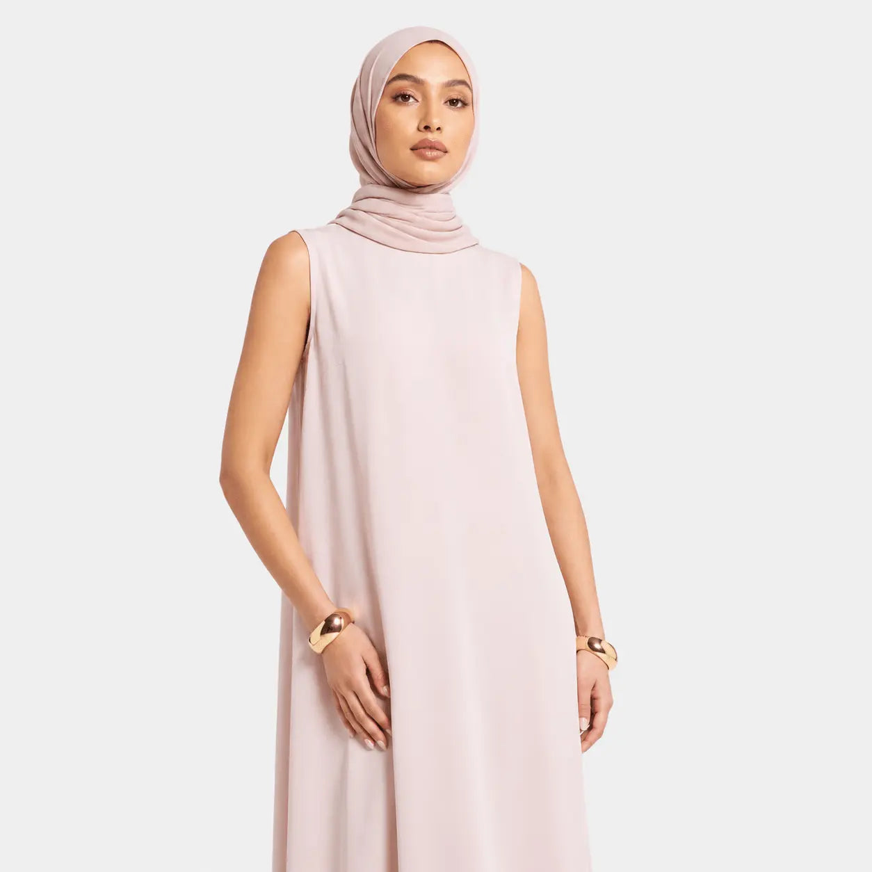 Woman wearing a light pink sleeveless dress and hijab on a white background