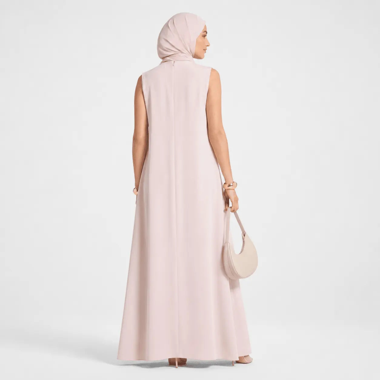 Woman wearing a long light pink dress and hijab on a white background