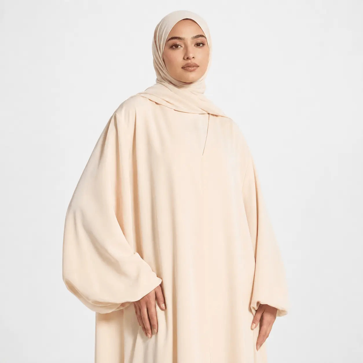 Woman wearing a beige abaya and hijab on a white background