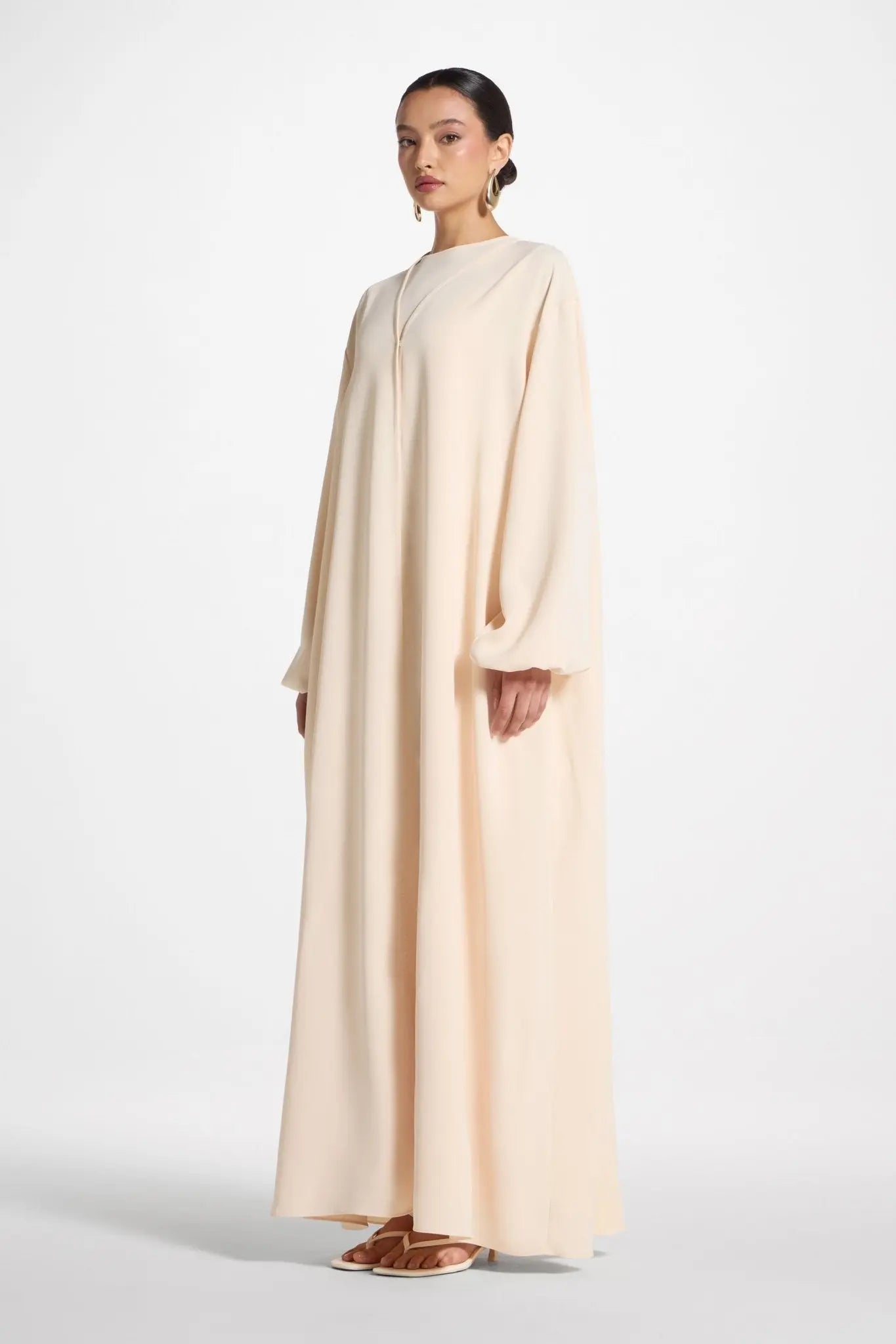 Woman wearing a long, light-colored dress on a white background
