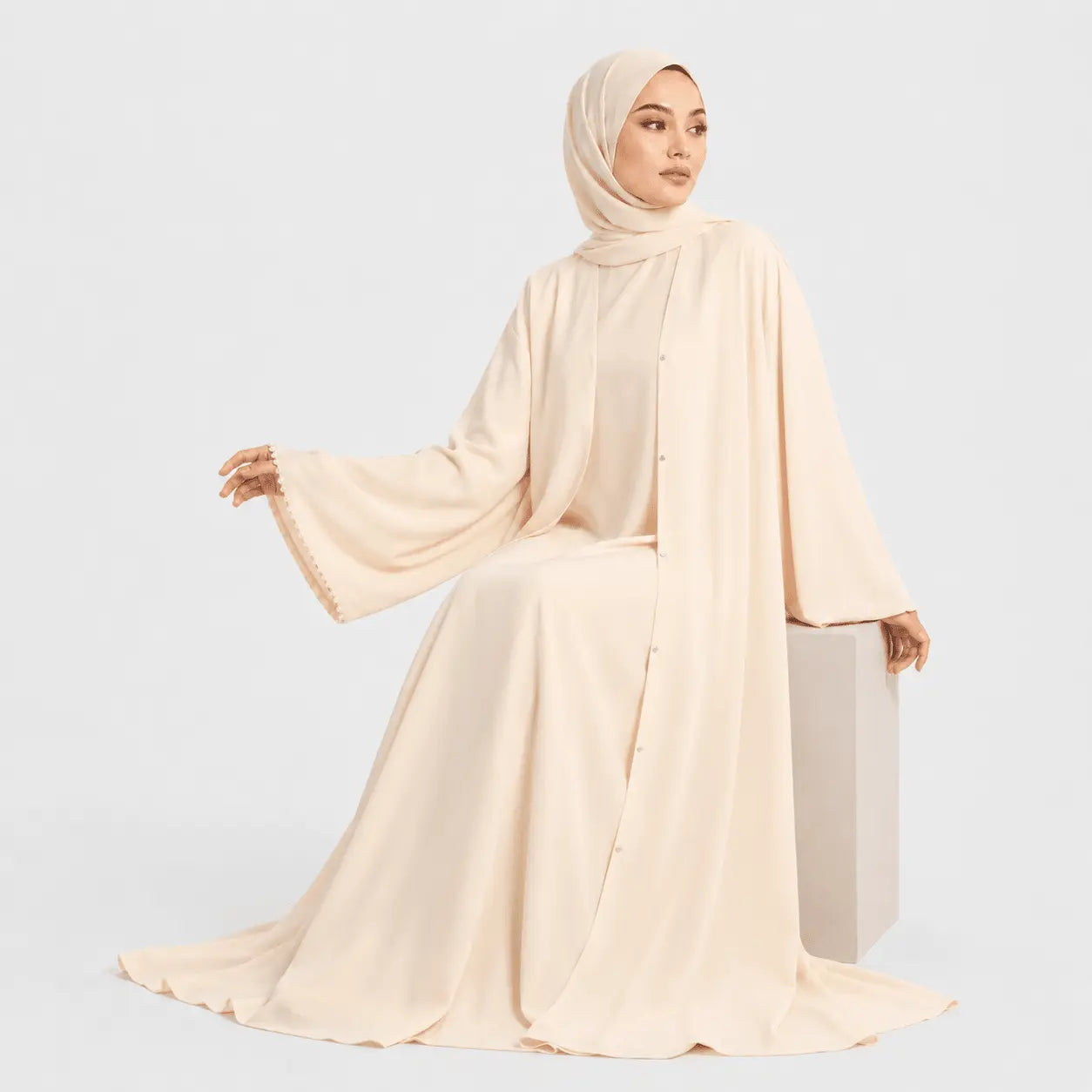 Woman wearing a beige abaya and hijab on a light gray background