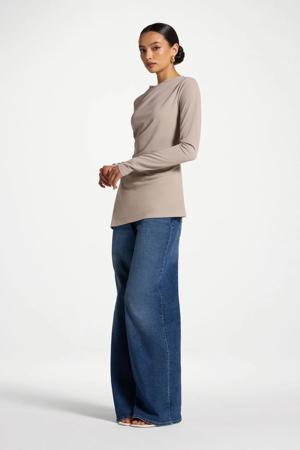 Woman wearing a beige long-sleeve top and blue jeans on a white background