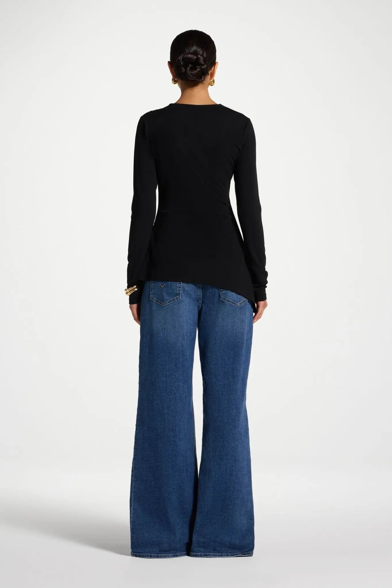 Person wearing a black long-sleeve top and blue jeans on a white background