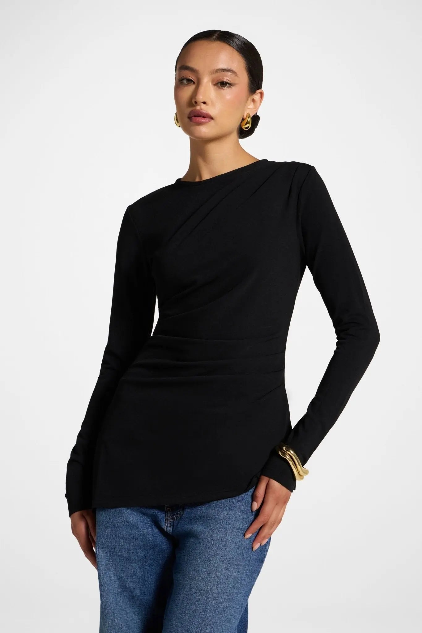 Woman wearing a black long-sleeve top and blue jeans on a white background