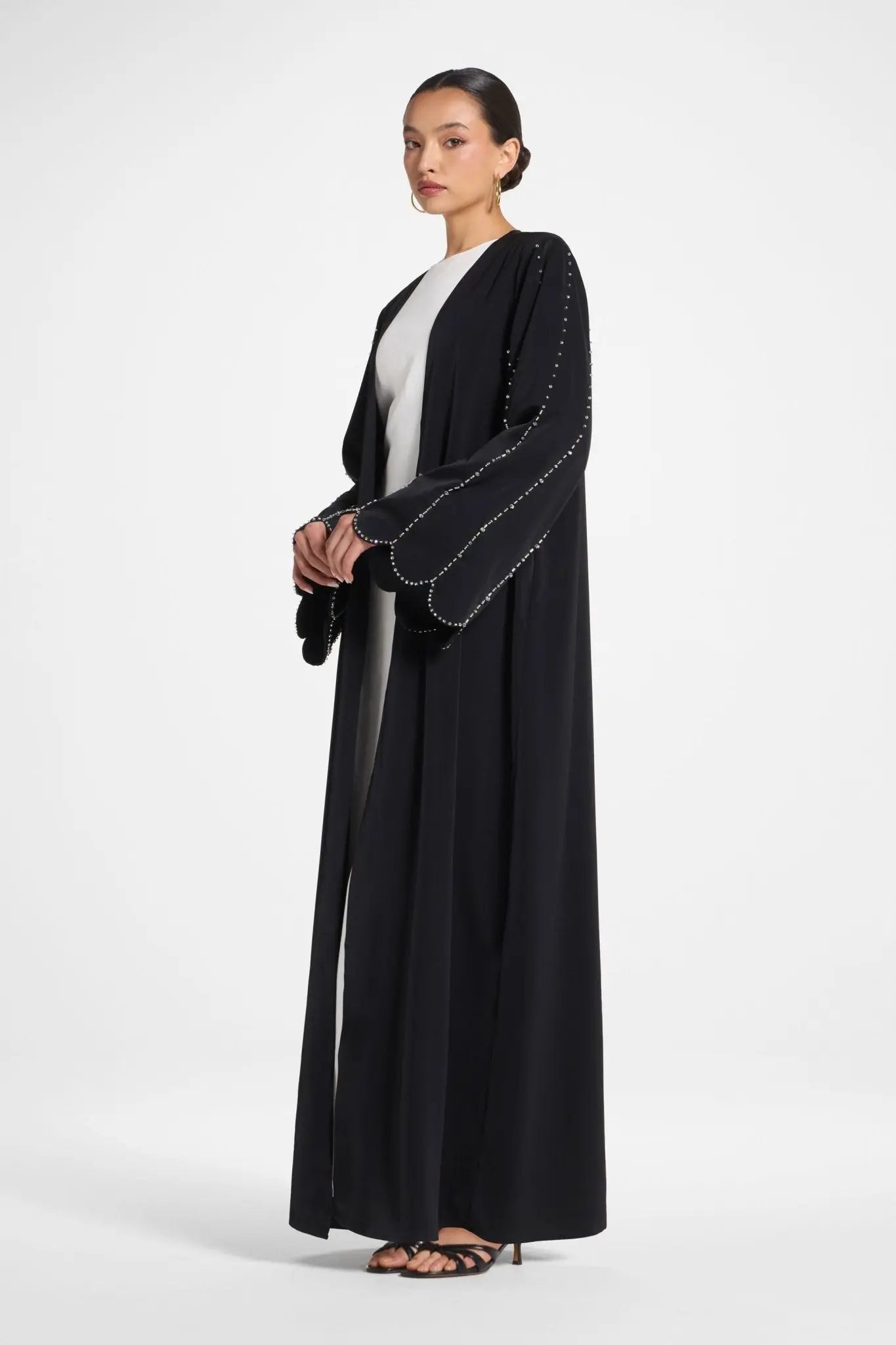 Woman wearing a black abaya with white trim on a white background