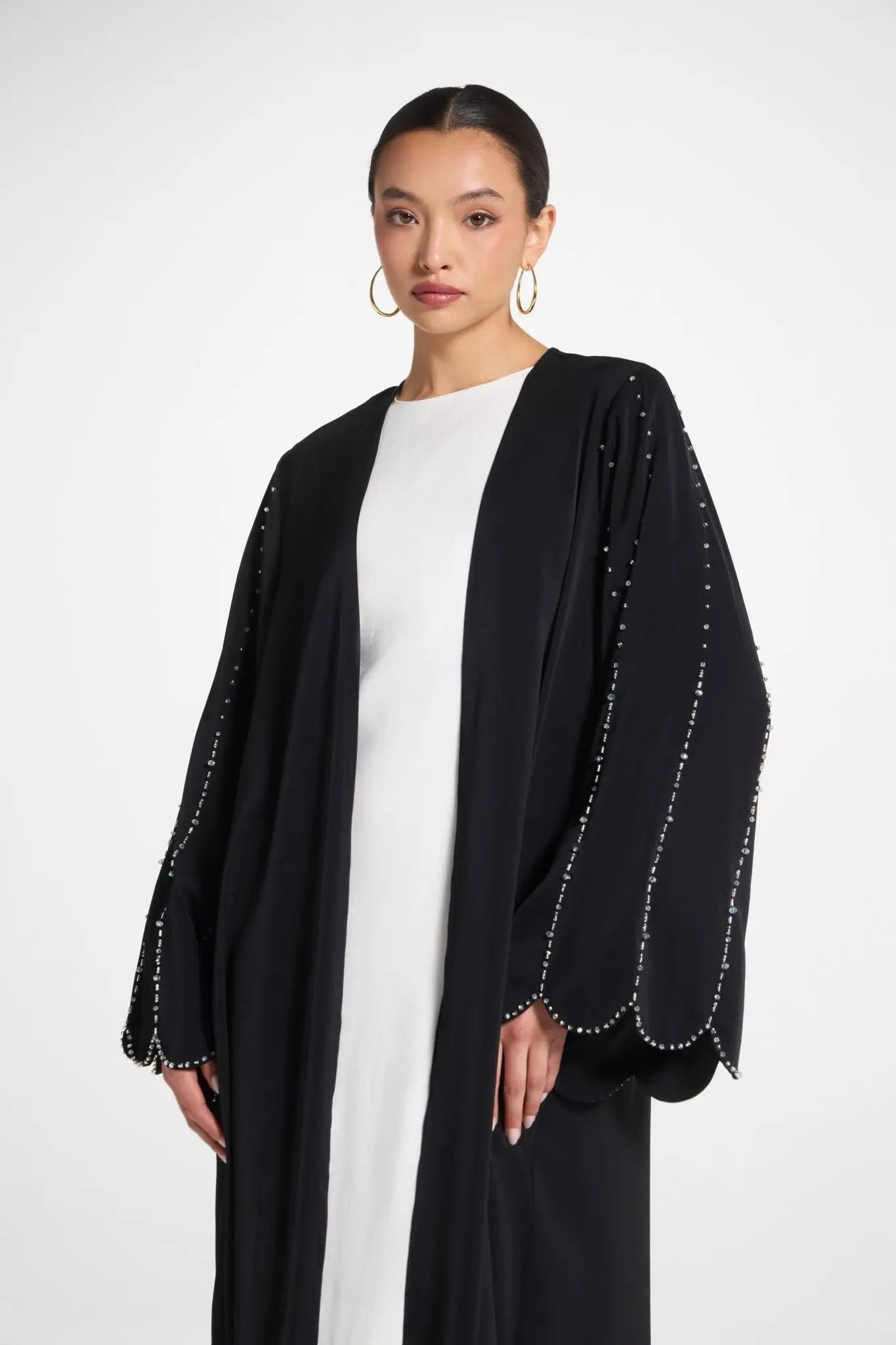Woman wearing a black abaya with white embellishments on a white background
