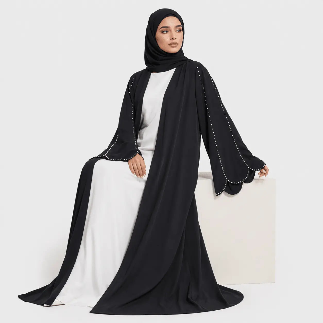 Woman wearing a black abaya with white trim on a white background