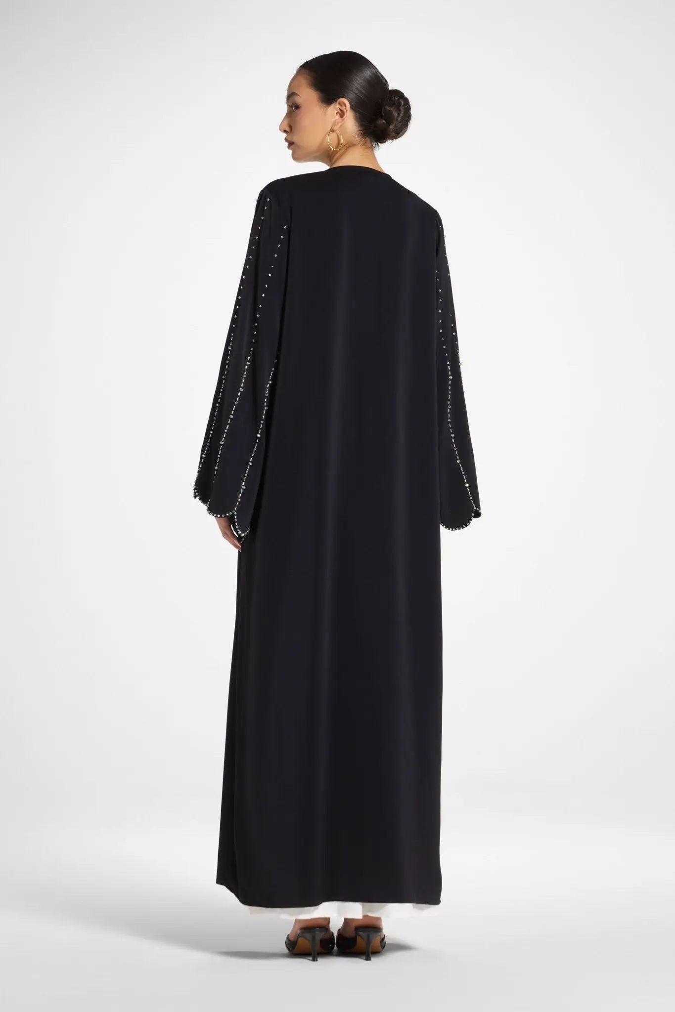Woman wearing a black abaya with embellished sleeves on a white background