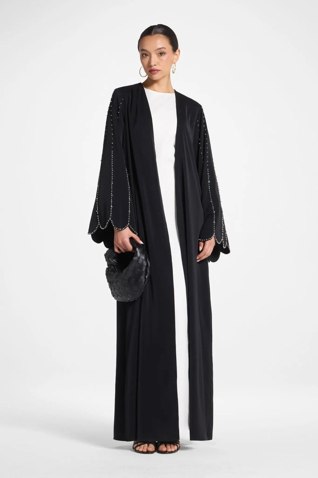 Woman wearing a black abaya with white trim on a white background