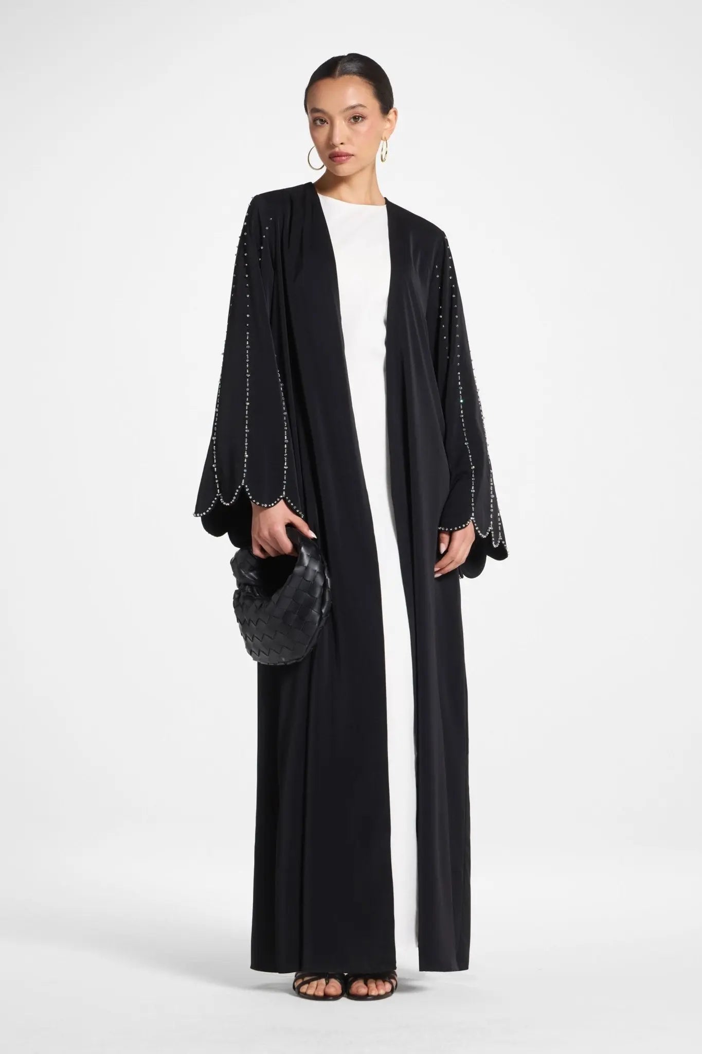Woman wearing a black abaya with white trim on a white background