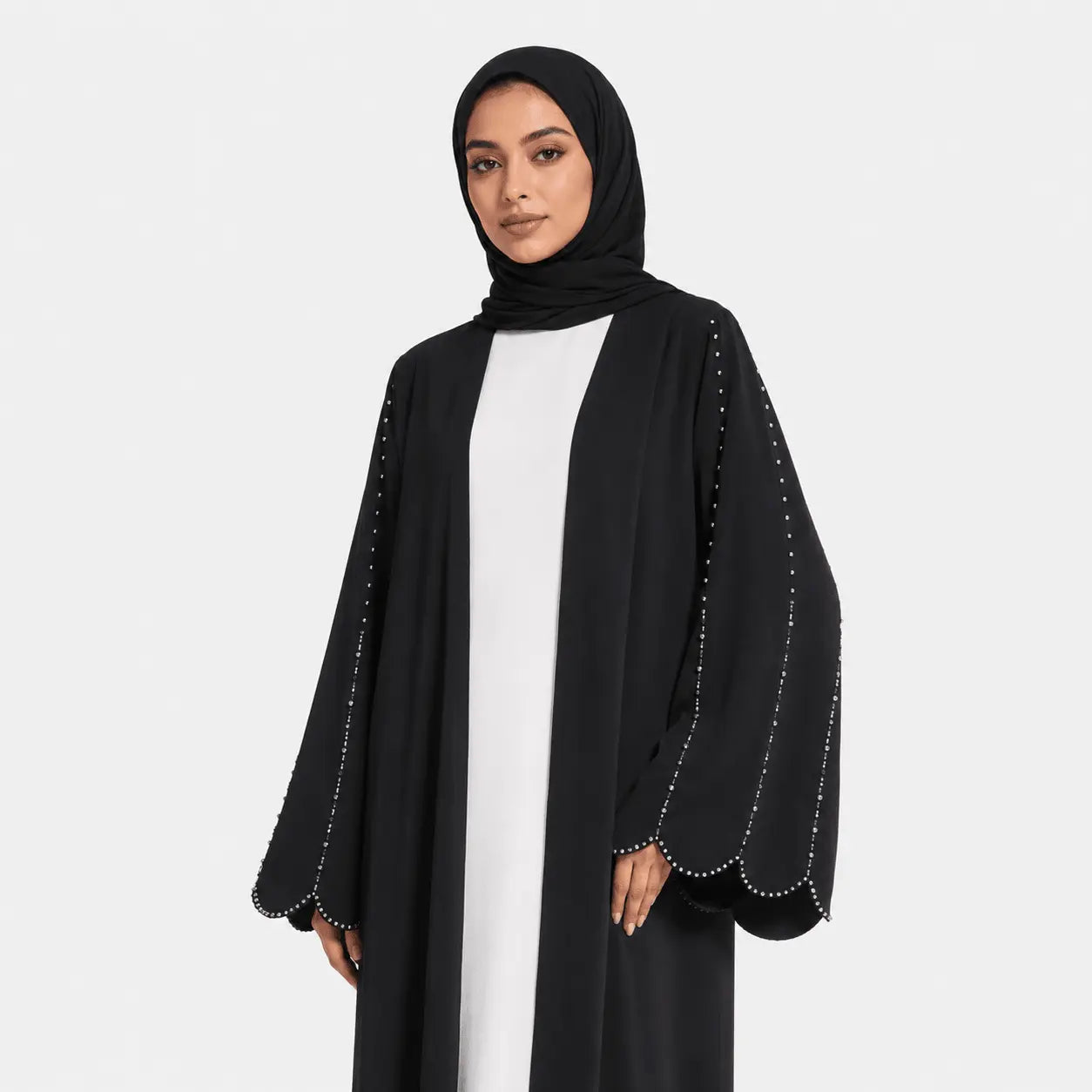 Woman wearing a black abaya with white inner garment on a light gray background