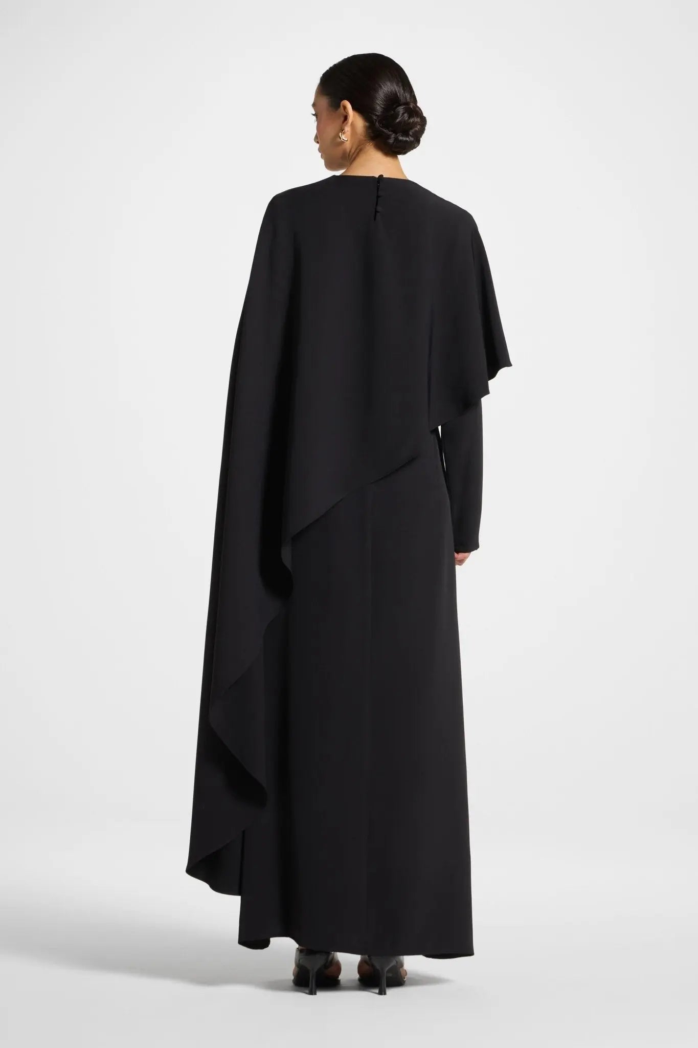 Person wearing a black dress with a cape on a white background