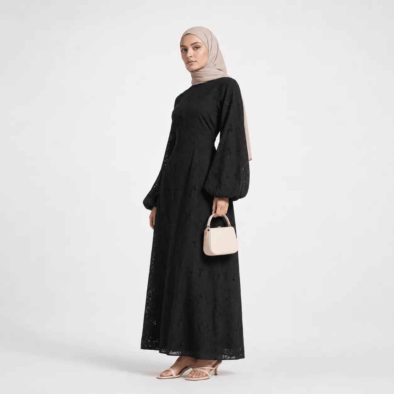 Woman in black lace modest dress with bell sleeves, beige hijab, and small handbag