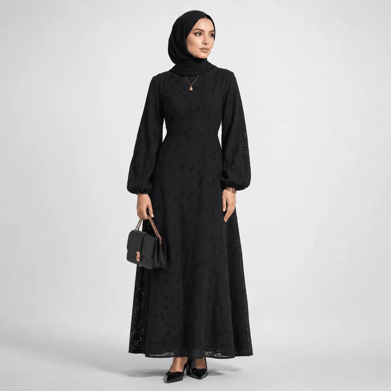 Elegant black lace maxi dress with puff sleeves, paired with hijab and small handbag for modest fashion.
