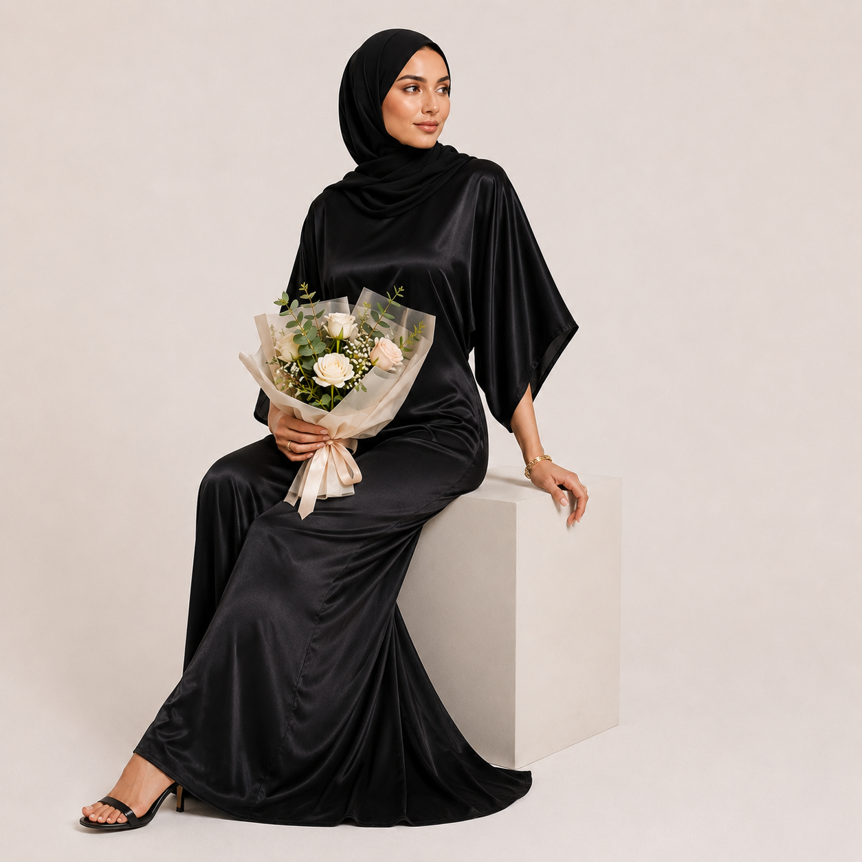 Woman in a black satin dress holding a bouquet of flowers against a plain background