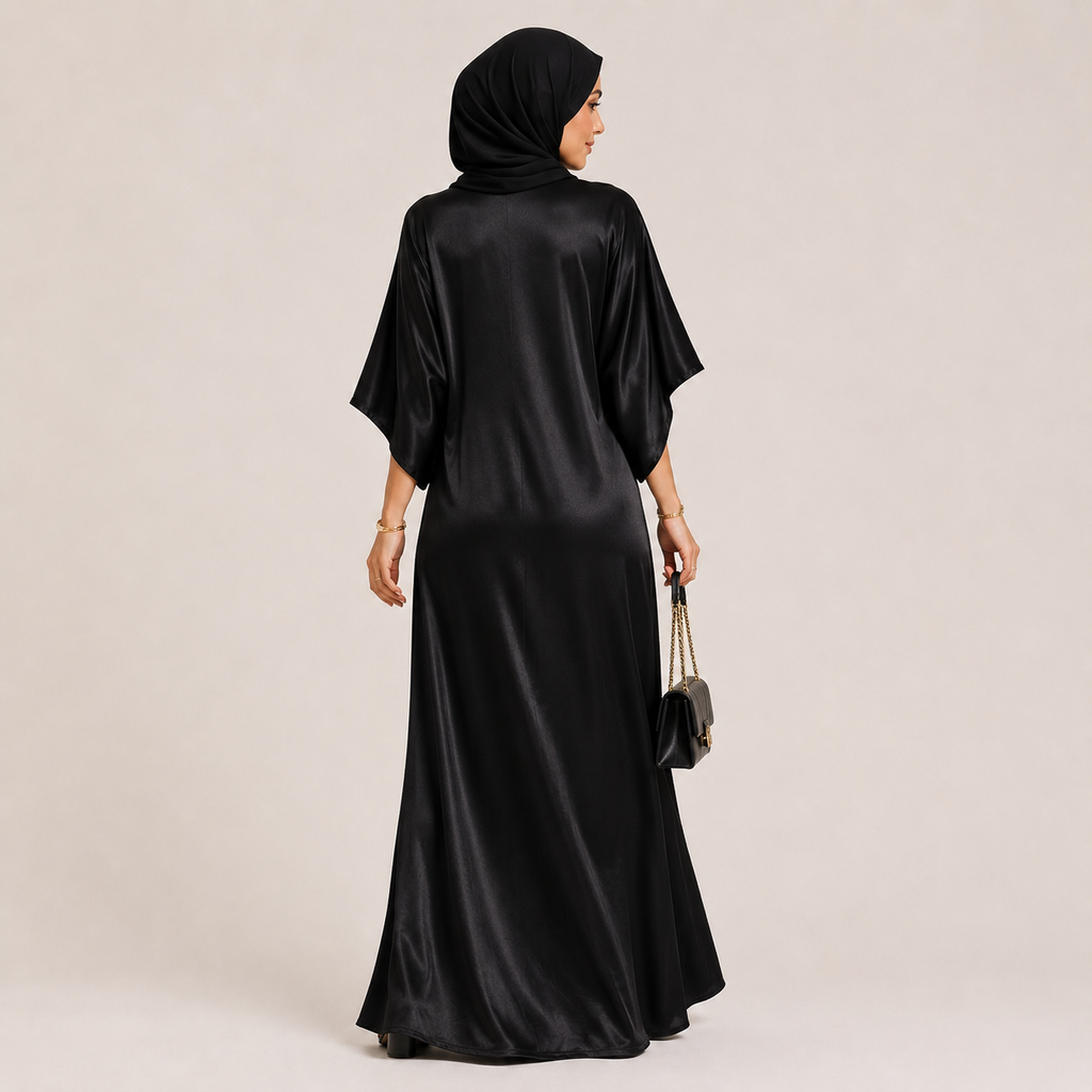 Woman wearing a black satin abaya with a matching hijab on a beige background