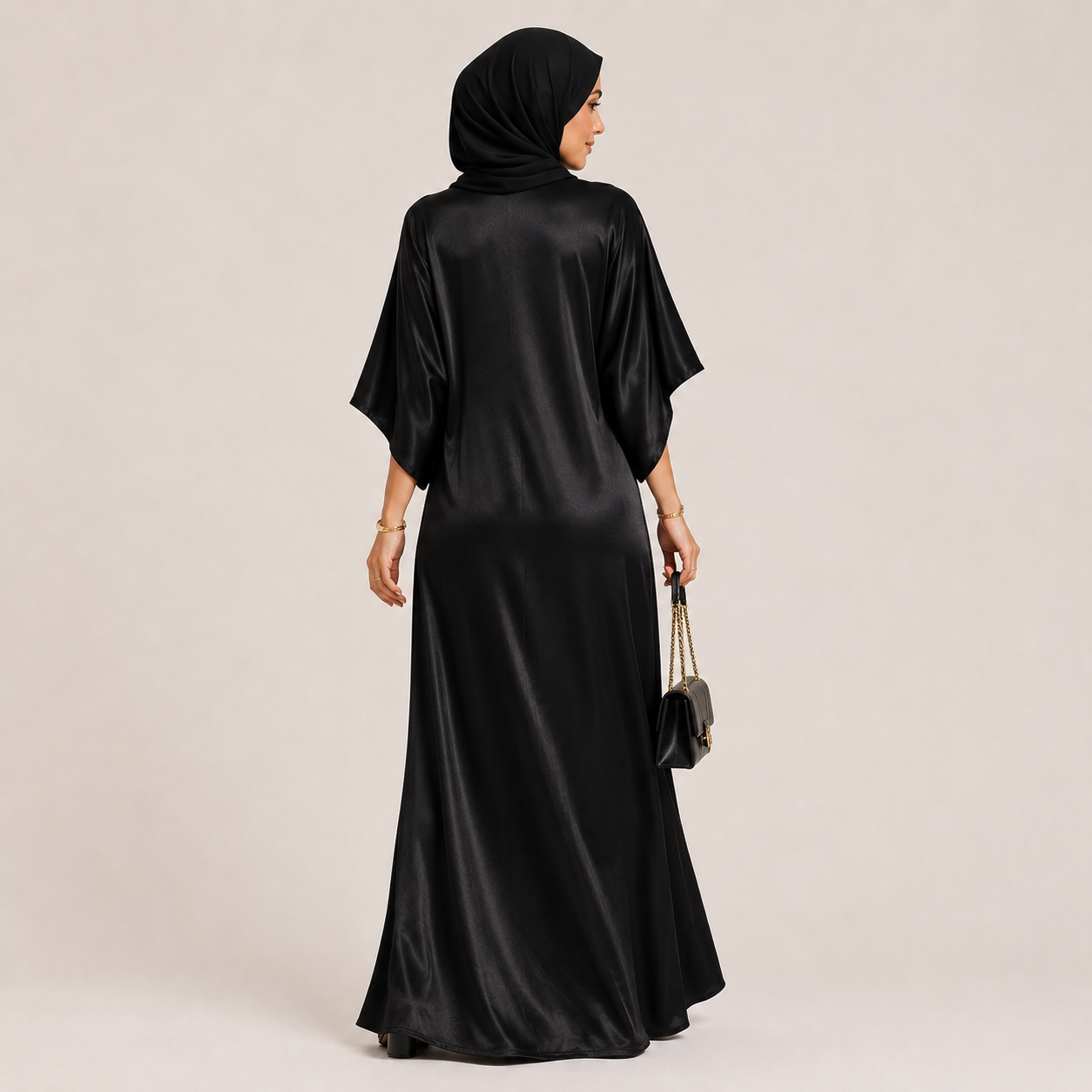 Woman wearing a black satin abaya with a matching hijab on a beige background