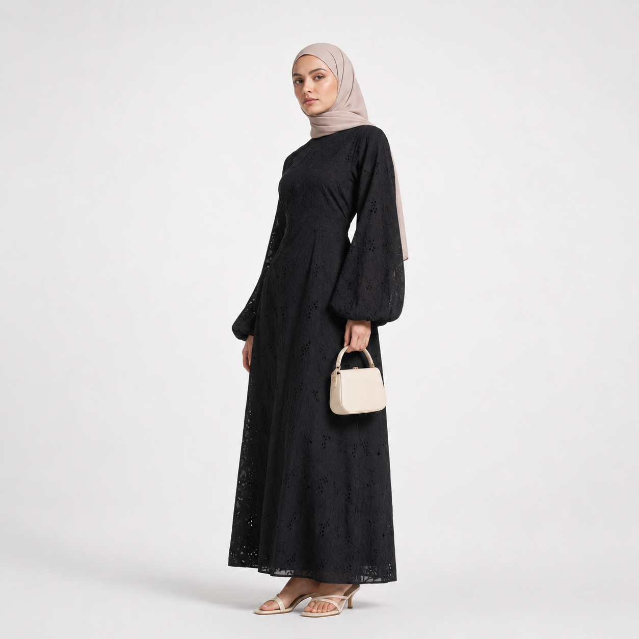 Woman wearing a black dress and beige hijab holding a beige handbag on a white background
